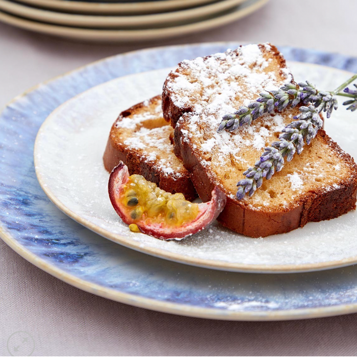 Two slices of pound cake, topped with powdered sugar, a lavender sprig, and half a passion fruit, served on Casafina/Costa Nova Brisa Sal Dinnerware from Portugal.