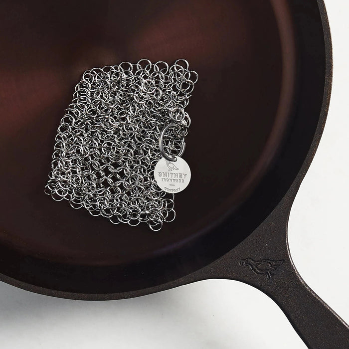 Smithey Ironware Chainmail Scrubber for cleaning cast iron cookware, with stainless steel mesh and sturdy handle.