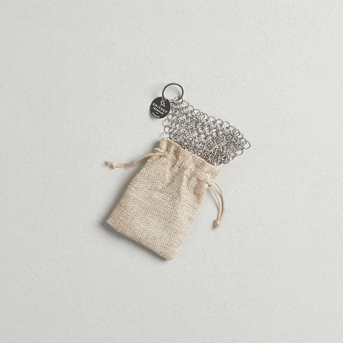 Smithey Ironware Chainmail Scrubber for cleaning cast iron cookware, showing the stainless steel chainmail scrubber on a black background.