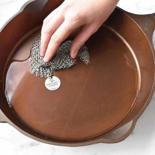 Smithey Ironware Chainmail Scrubber for cleaning cast iron cookware, with stainless steel mesh and handle for effective scrubbing.