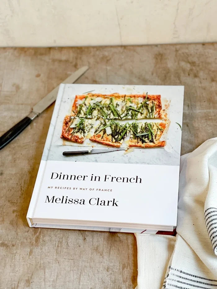 Dinner in French cookbook by Melissa Clark, featuring French-inspired dishes, open to a page with a colorful recipe and images.