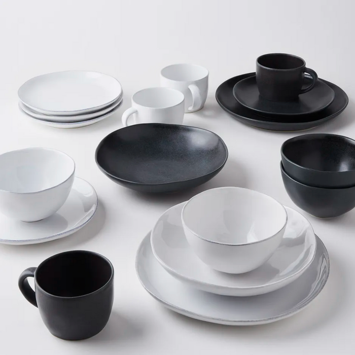 The Livia Dinnerware Matte Black collection by Casafina/Costa Nova features stoneware plates, bowls, and cups in black and white, arranged in matching pairs on a white surface.