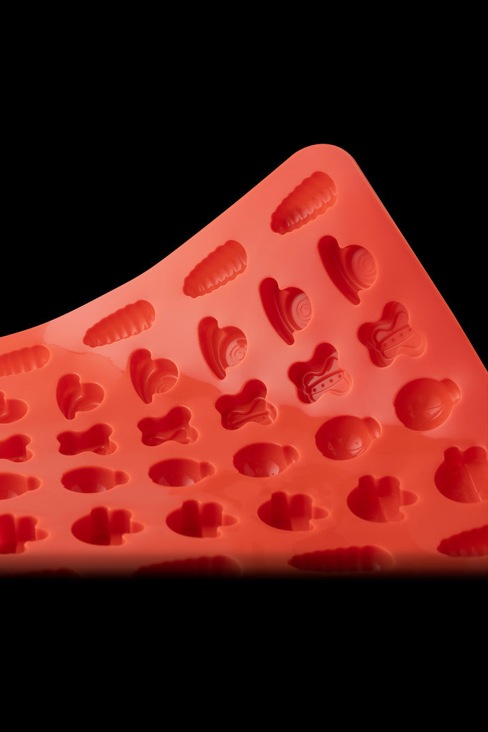 Red silicone mold with various cannabis-themed shapes, including leaves, gummies, and characters.