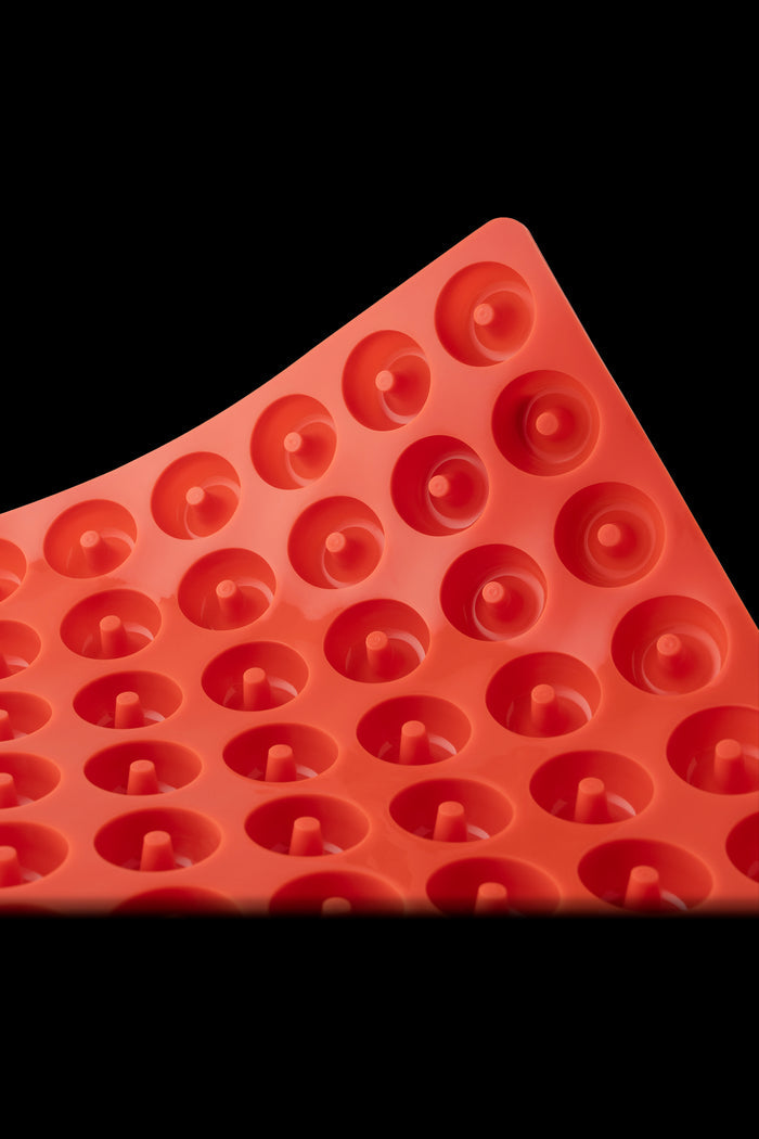 Close-up of a red silicone concentrate collection mat with circular wells.