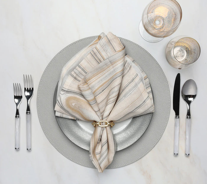 Elegant table setting features a gray and white plate, striped napkin with a gold ring, cutlery, and glasses—all arranged on the Kim Seybert Shagreen Placemat Elephant Grey Set of 4 atop a white surface.