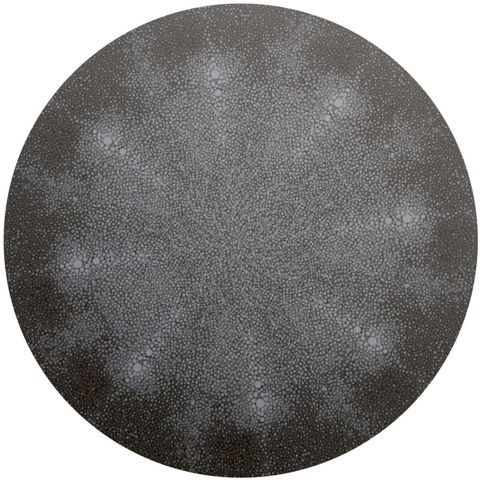 The Shagreen Placemat by Tisch New York features an intricate, circular design of small white cell-like dots radiating symmetrically from the center, creating a textured starburst effect on a dark gray background.